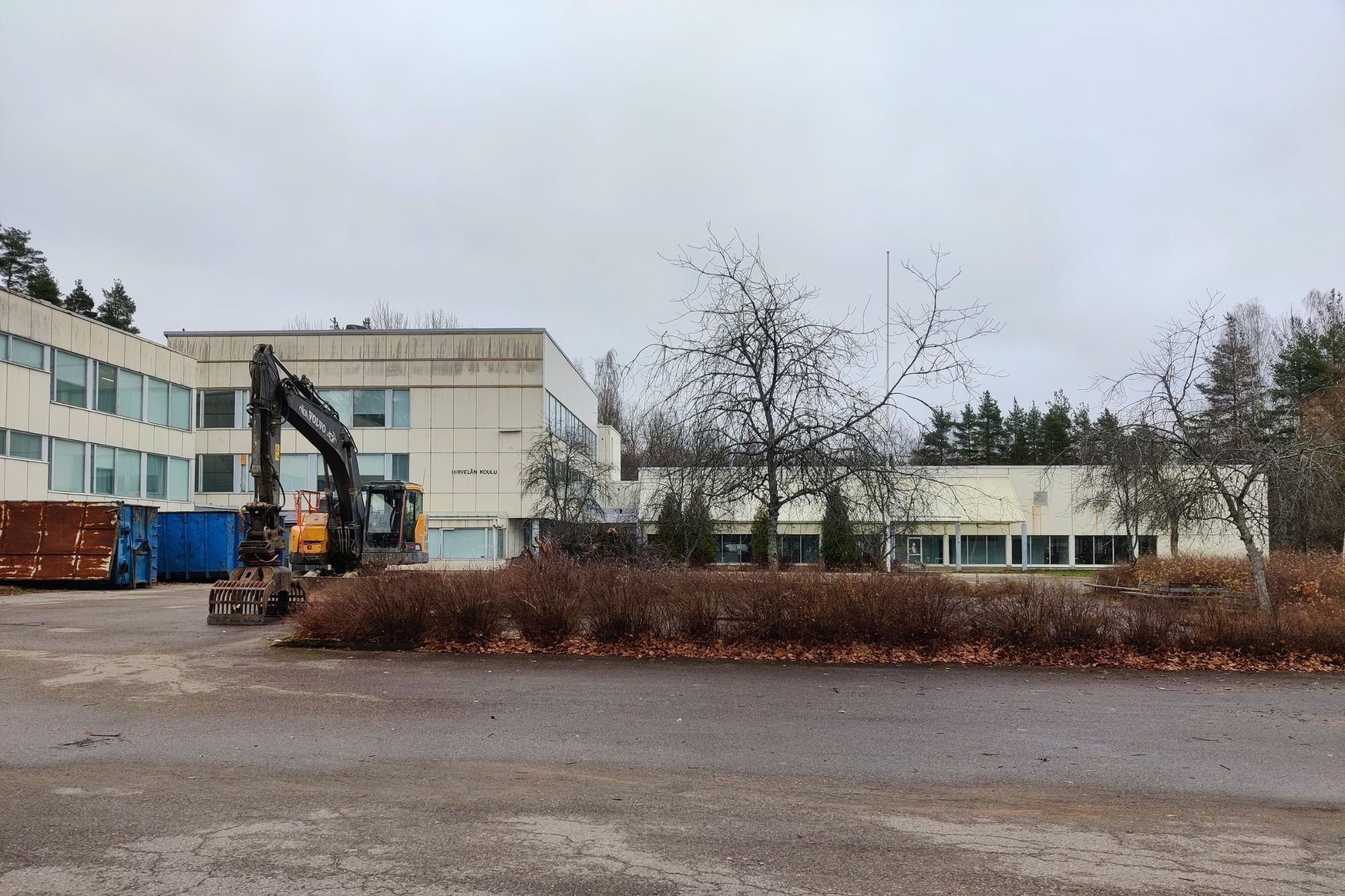 Koulurakennus, syksyinen ilma ja parkkipaikalla työkoneita.